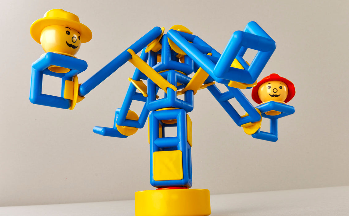 Toy figure on a blue and yellow seesaw with a plain background