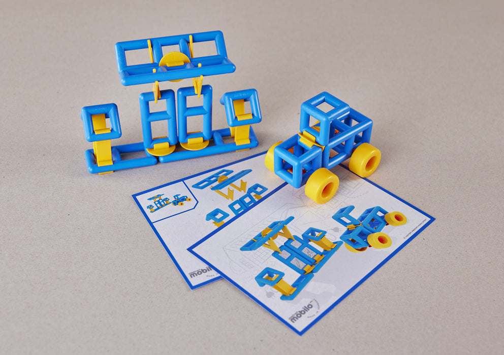 Blue and yellow plastic building blocks arranged to form a small vehicle and a separate frame structure, with two printed instruction sheets placed in front on a light beige surface.