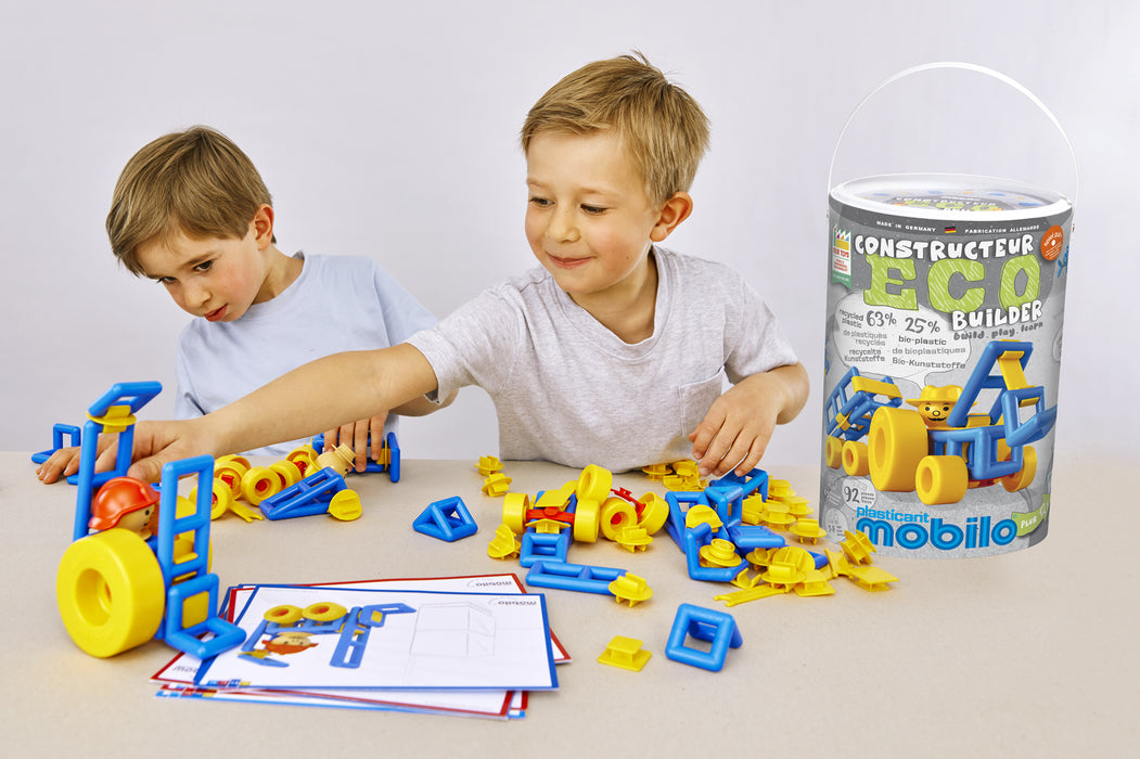 Two children playing with a toy construction set on a table, with a container labeled 'Mobiloo' in the background.