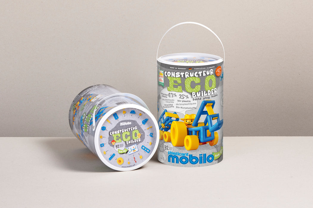 Two cylindrical toy bins for the Mobilo Constructeur Eco Builder, one standing upright and one lying on its side, on a light beige surface against a neutral beige background.